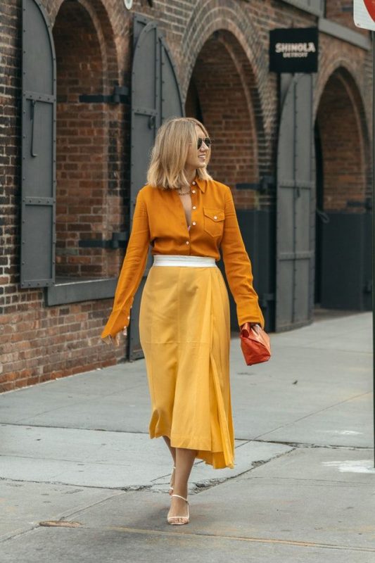 Cô gái mặc áo khoác cam đất và quần ống rộng vàng, phong cách năng động.