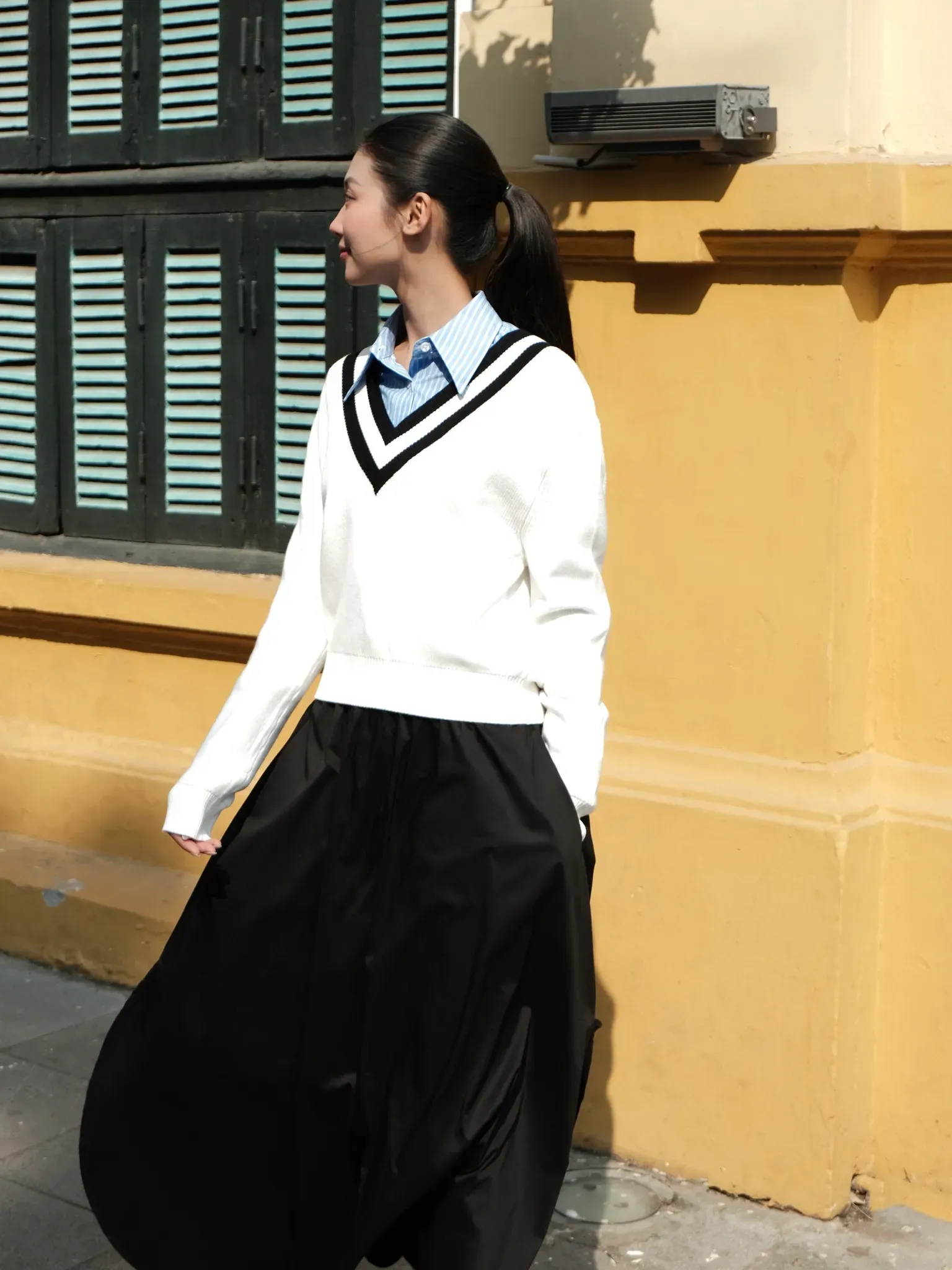 Outfit kết hợp áo len trắng với kiểu dáng trẻ trung và chân váy đen dài, mang đến sự thanh lịch và tối giản